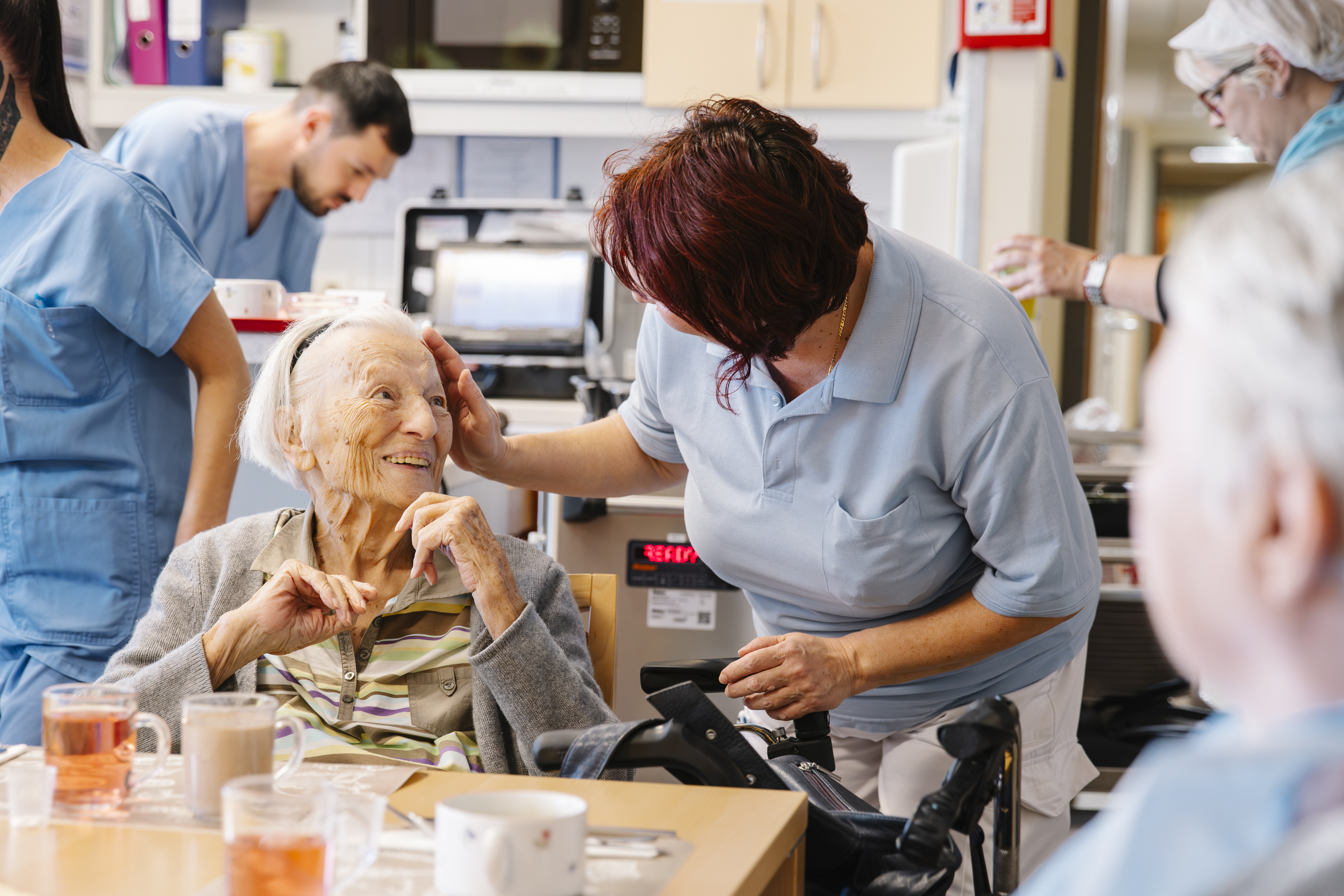 Eine Pflegekraft streichelt einer älteren Dame liebevoll über die Wange.