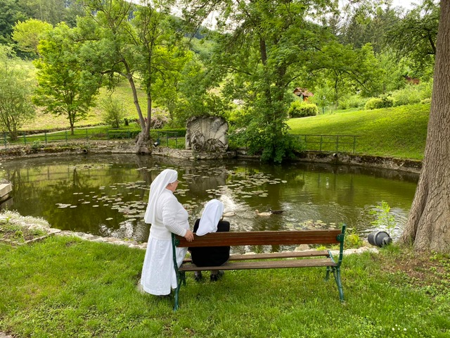 Zwei Ordensschwestern sitzen auf einer Gartenbank vor dem Teich