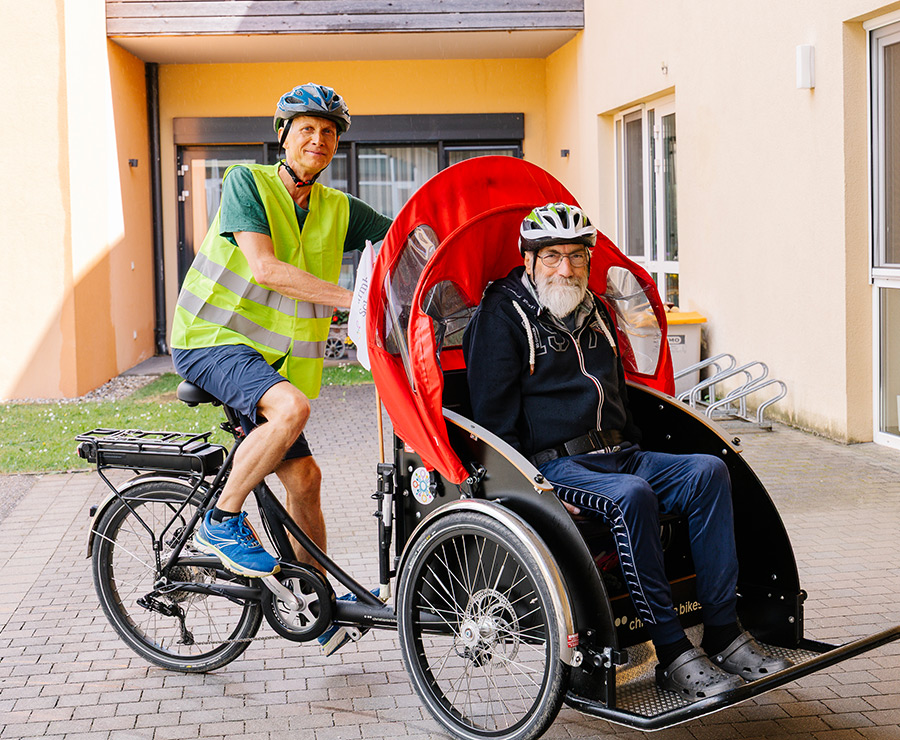 Ein Ehrenamtlicher fährt mit eine Bewohner mit der E-Bike-Rikscha.