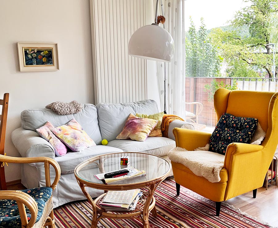 Ein gemütlich eingerichtetes Wohnzimmer mit Couch, Ohrensessel und Blick ins Grüne.