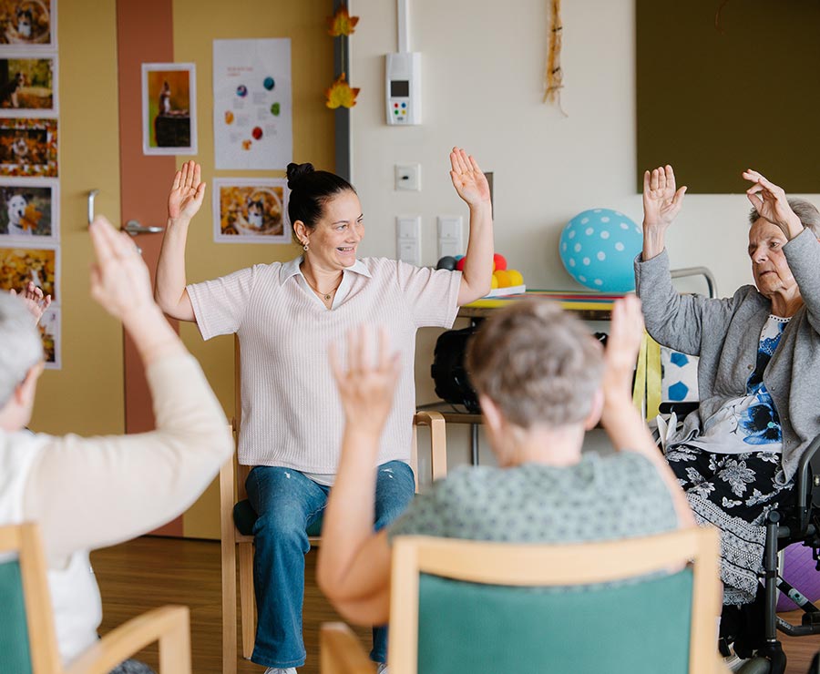 Eine Seniorenbetreuerin bei der Bewegungsrunde mit Bewohnerinnen und Bewohnern im Pflegehaus