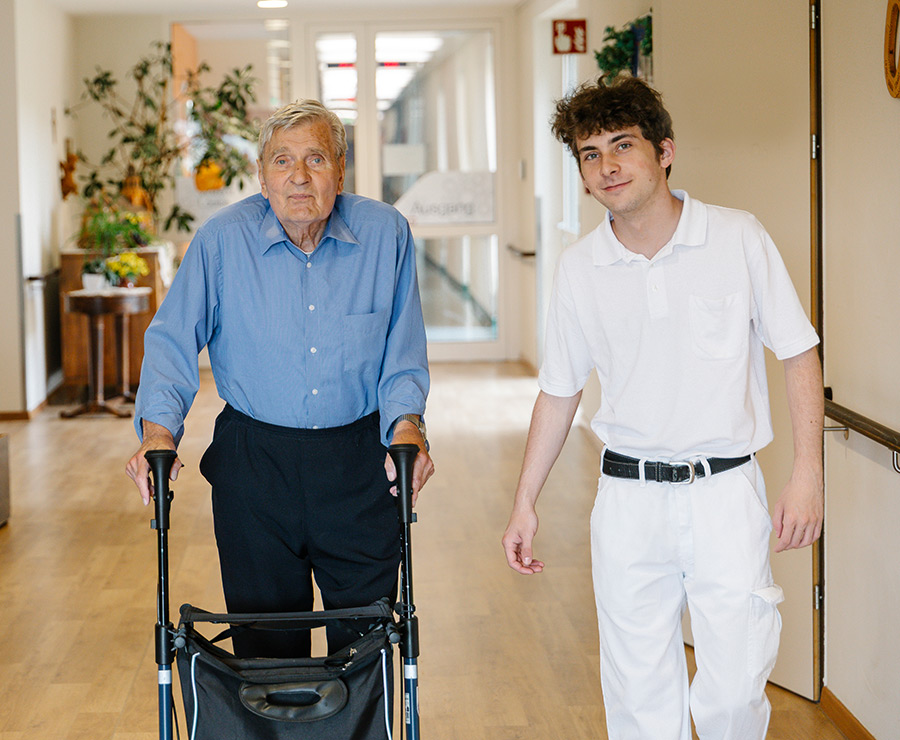 Ein Zivildiener und ein Bewohner mit Rollator gehen gemeinsam spazieren