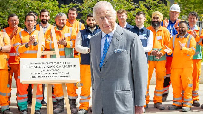 King Charles stands beside a commemorative plaque on an easel.