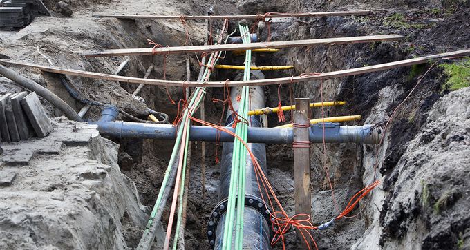 Excavated trench with a large blue pipe and bundled green and orange utility cables