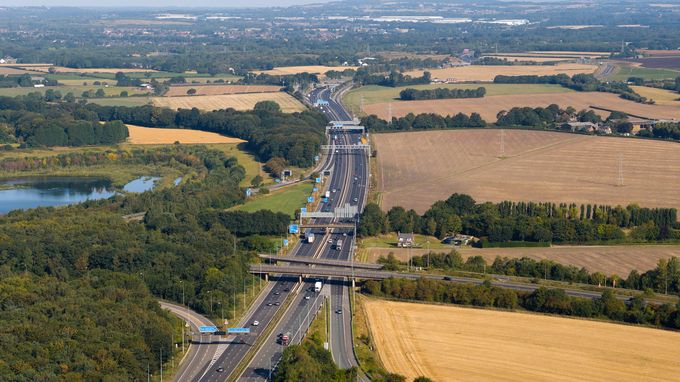 Panoramic aerial view of the M6 motorway near Croft Interchange in Warrington, running through golden farmlands and green woodlands