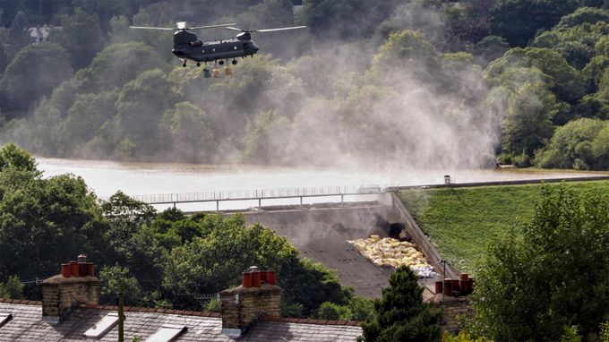 Chinook helicopter hovering low over a dam, about to drop bags of aggregate