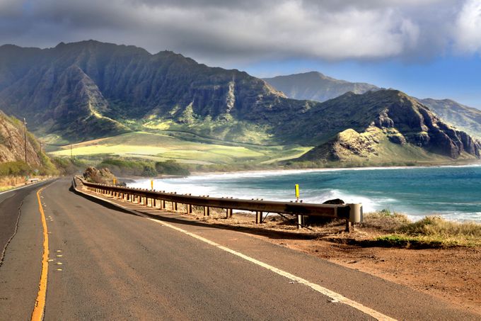 Winding coastal road with guardrail beside turquoise ocean and sandy shore