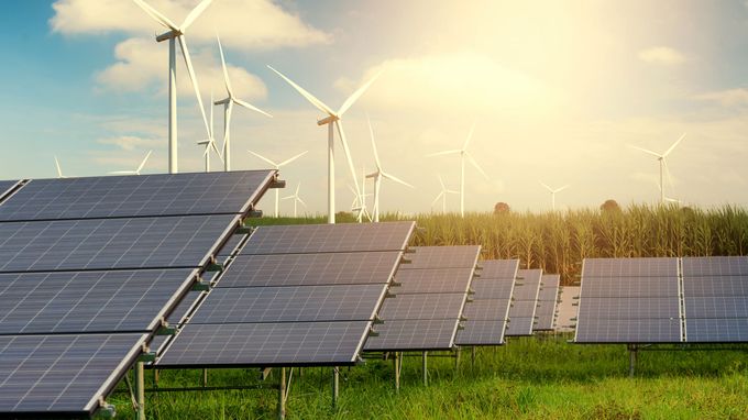Rows of solar panels in a grassy field with wind turbines on the horizon
