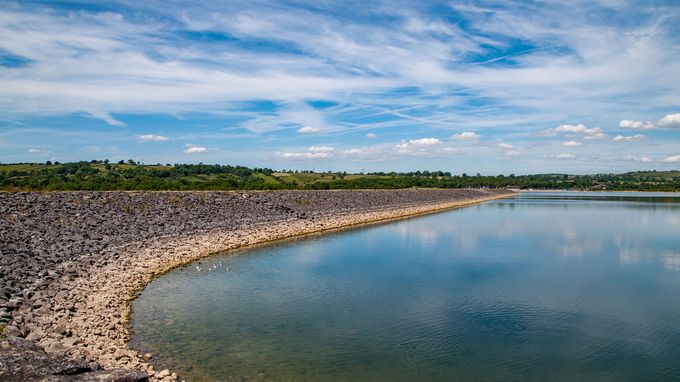 Curved rocky embankment along a calm reservoir with blue sky
