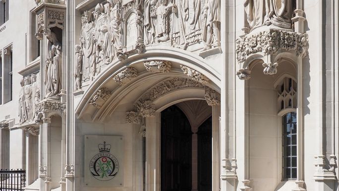 Ornate entrance of a historical building with detailed stone carvings and a sign displaying a crown and floral emblem.