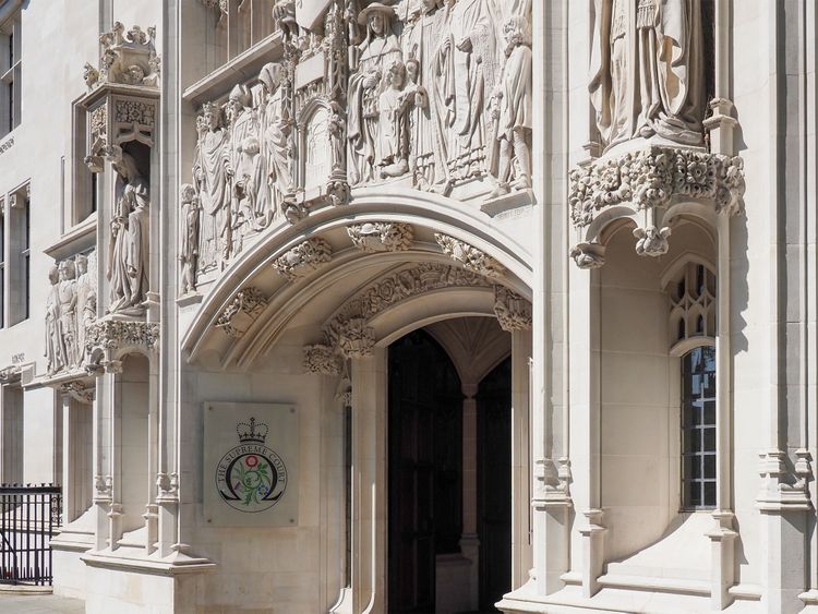 Ornate entrance of a historical building with detailed stone carvings and a sign displaying a crown and floral emblem.