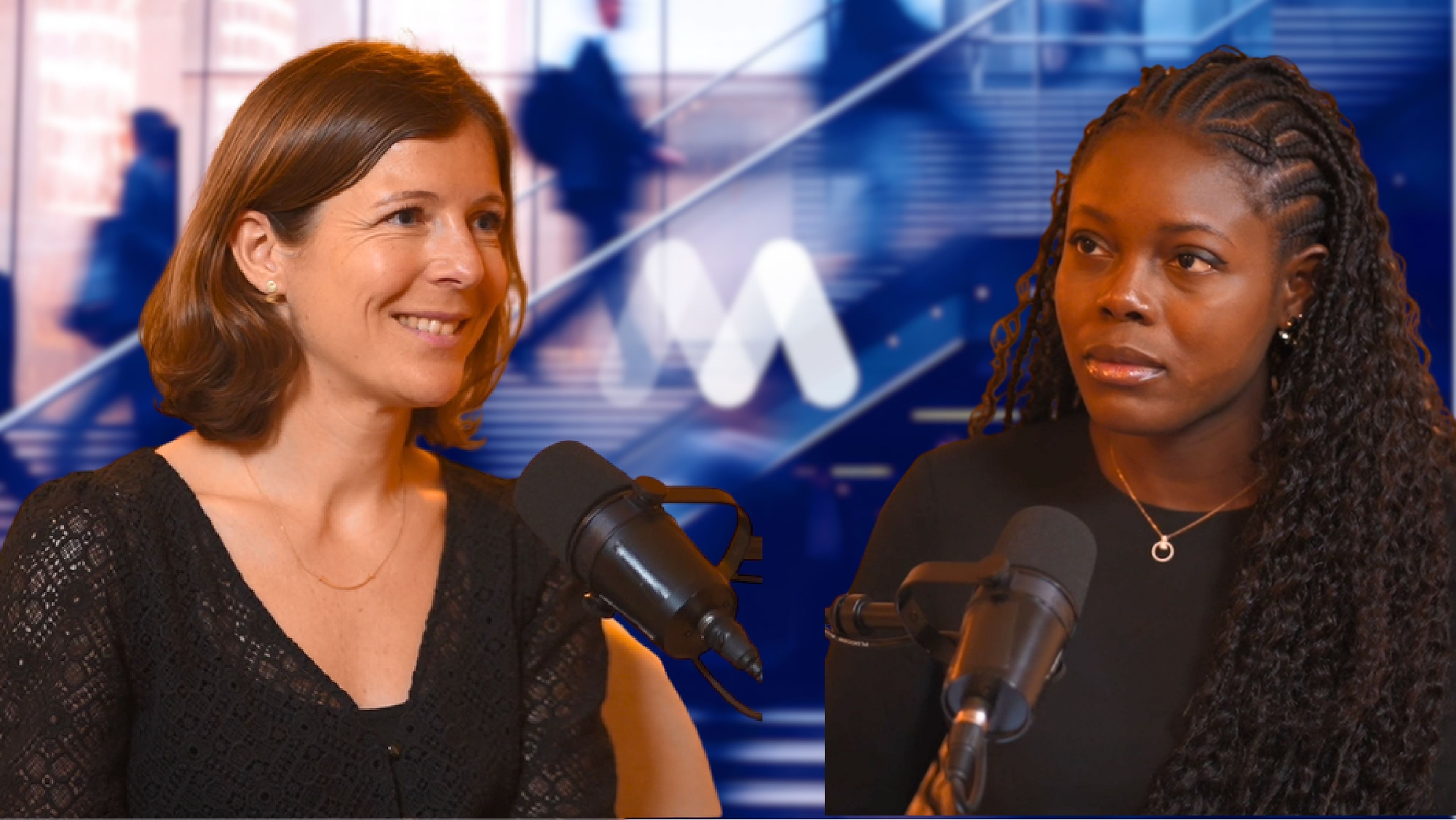 Two women with microphones have a conversation against a blurred background with stairs and silhouettes.