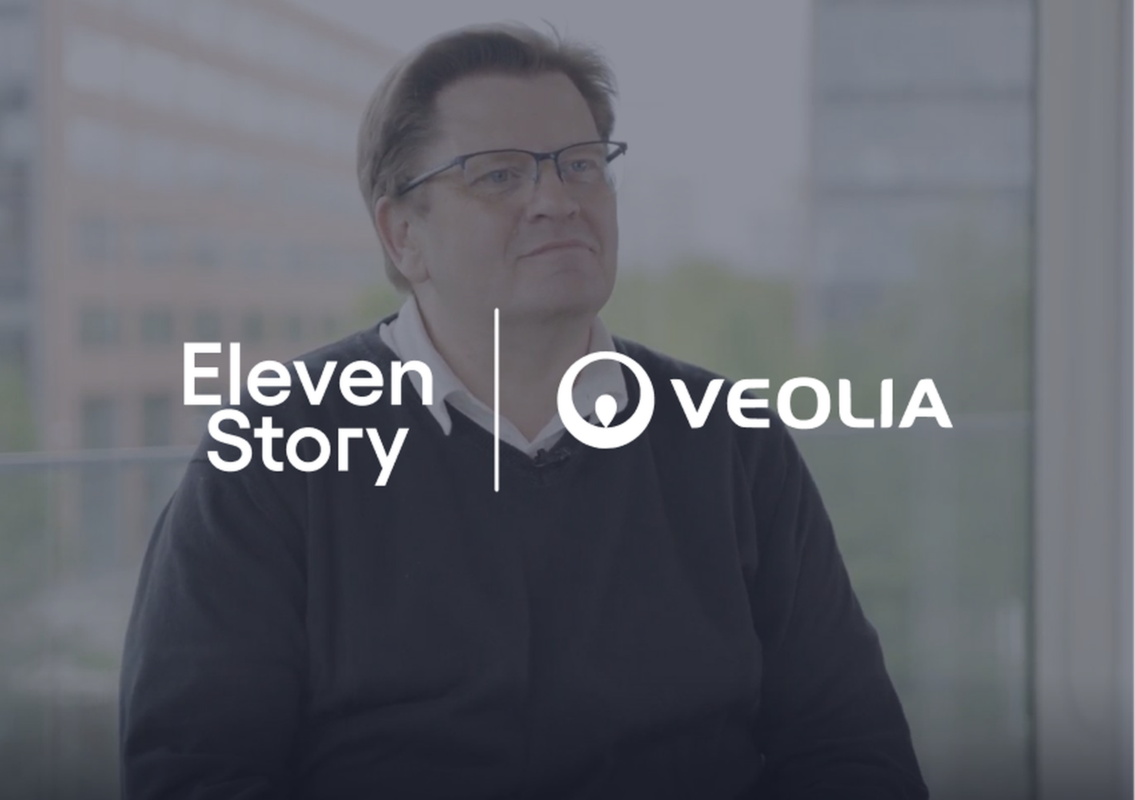A man wearing glasses and a dark sweater sits indoors with a city view. Logos of Eleven Story and Veolia overlay on the image.
