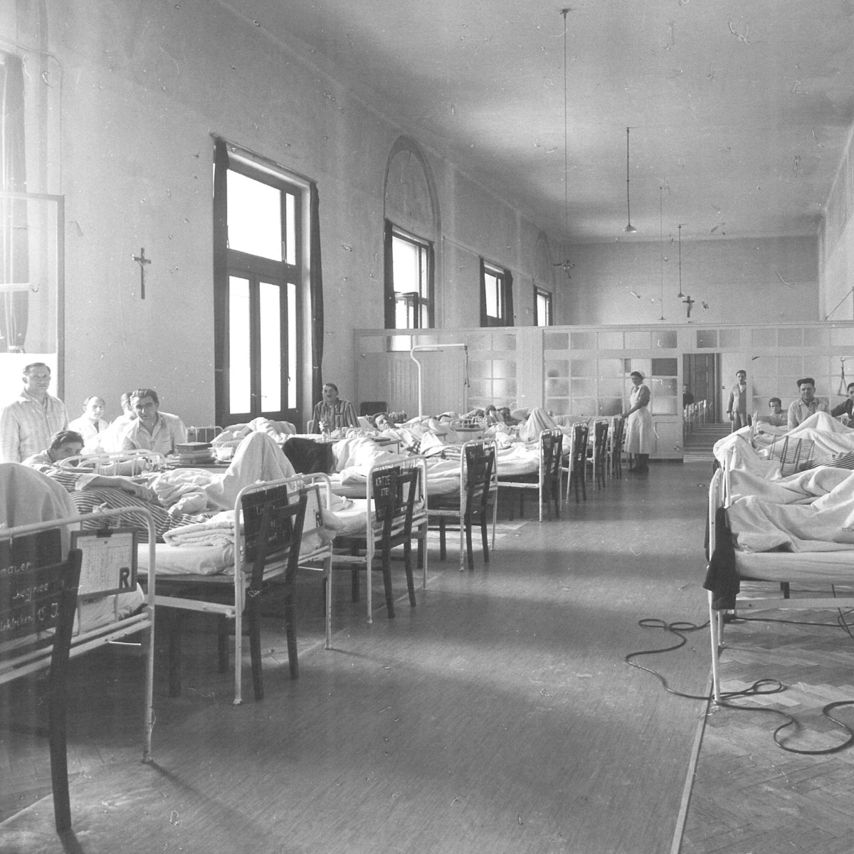 Eine historische Schwarz-Weiß-Aufnahme einer Krankenstation. Mehrere Betten sind aneinandergereiht.