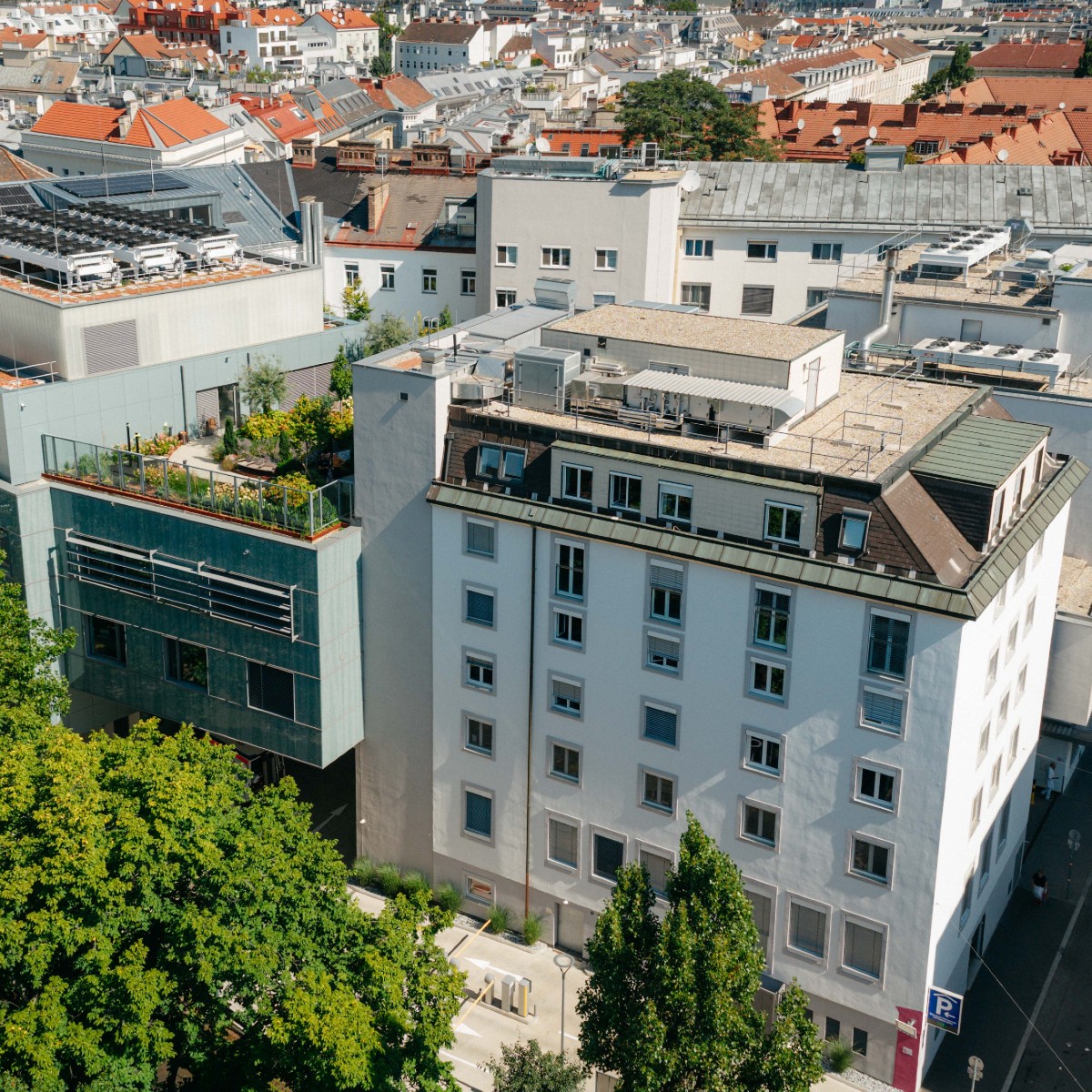 Eine Außenaufnahme des Herz-Jesu Krankenhauses Wien. Zu sehen sind eine begrünte Terrasse und Bäume, die das Krankenhausgebäude säumen.