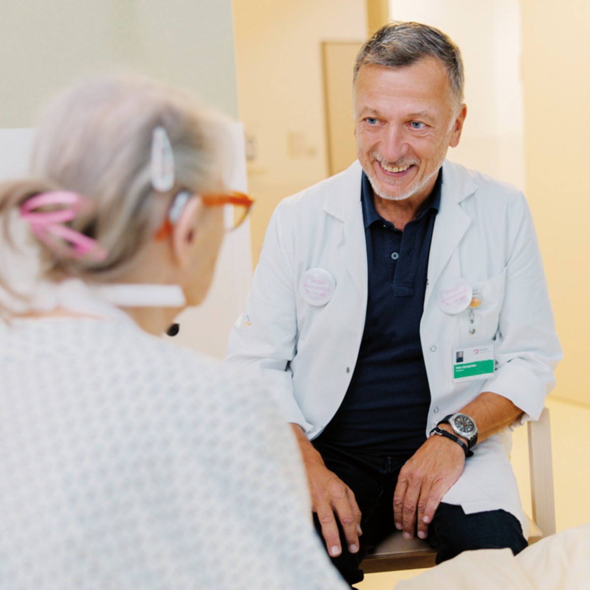 Gesprächssituation zwischen einem Arzt im Kittel und blauem Polo, der mit einer Patientin spricht