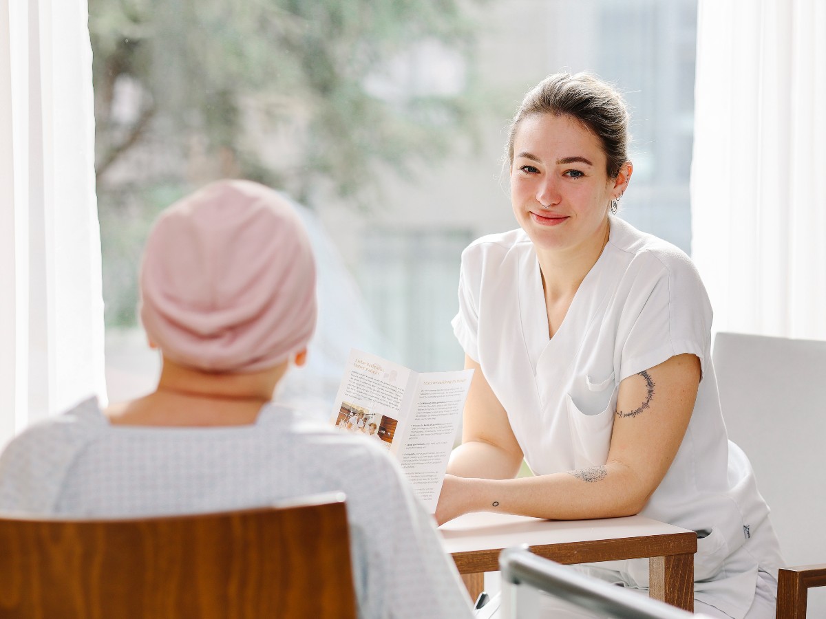 Eine junge Gesundheitsfachkraft sitzt an einem Tisch mit einer Person
