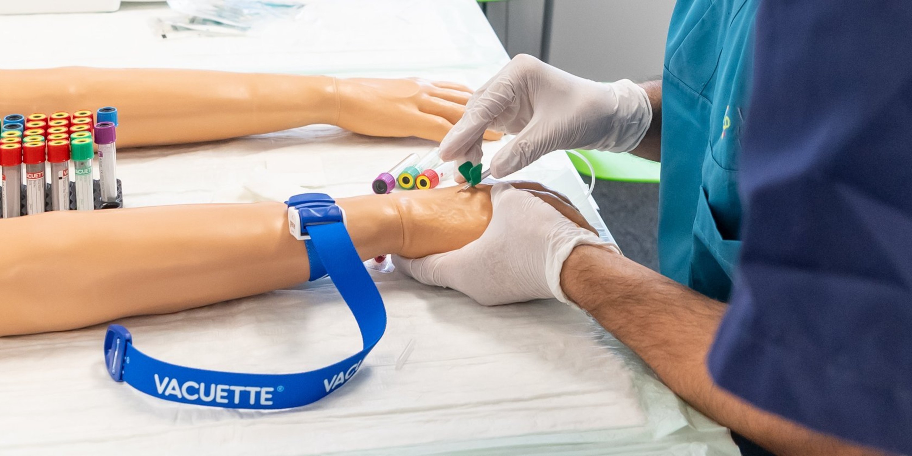 Nahaufnahme von Schüler*innen, die an einer Handattrappe das setzen einer Infusion üben. 