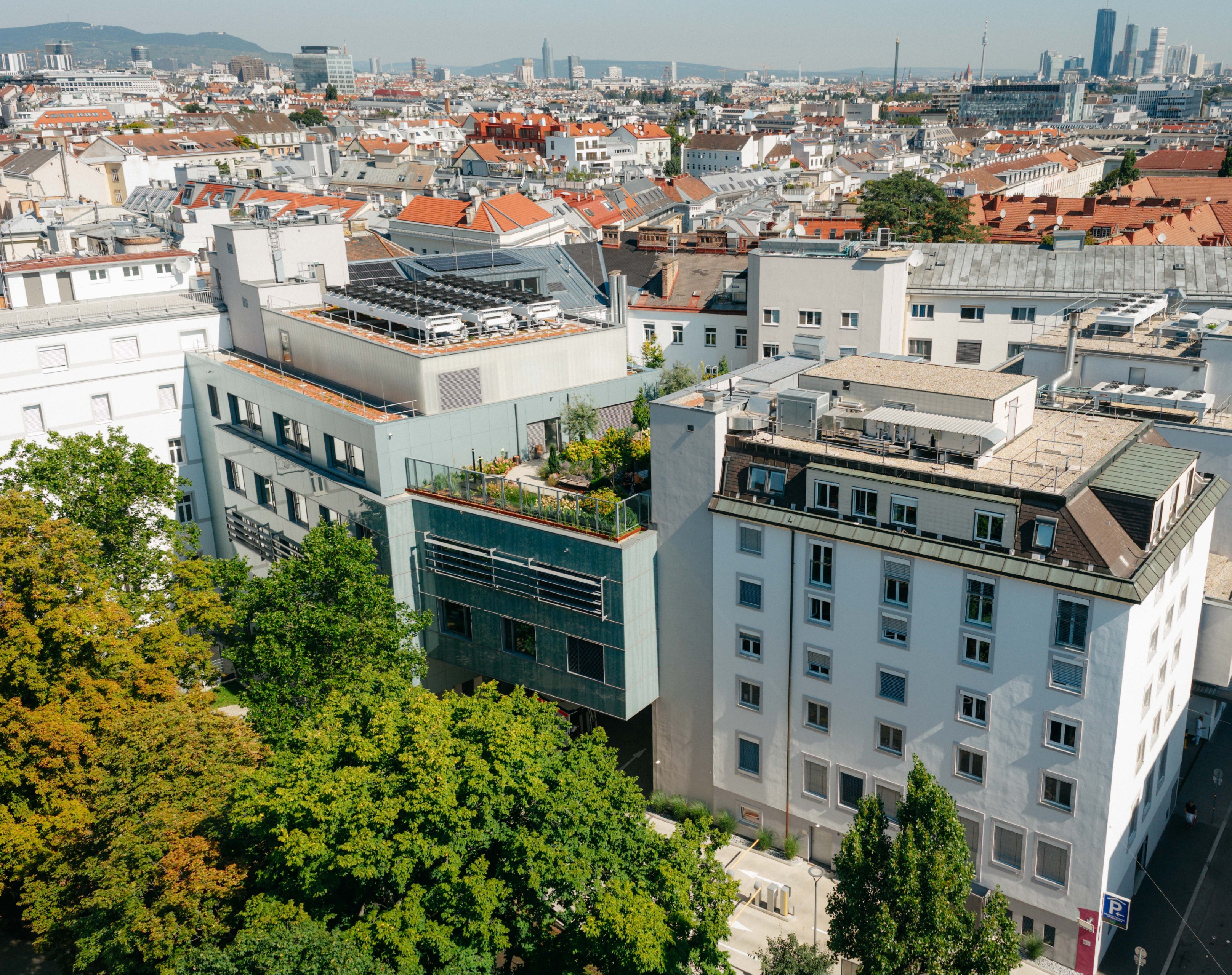 Eine Außenaufnahme des Herz-Jesu Krankenhauses Wien. Zu sehen sind eine begrünte Terrasse und Bäume, die das Krankenhausgebäude säumen.