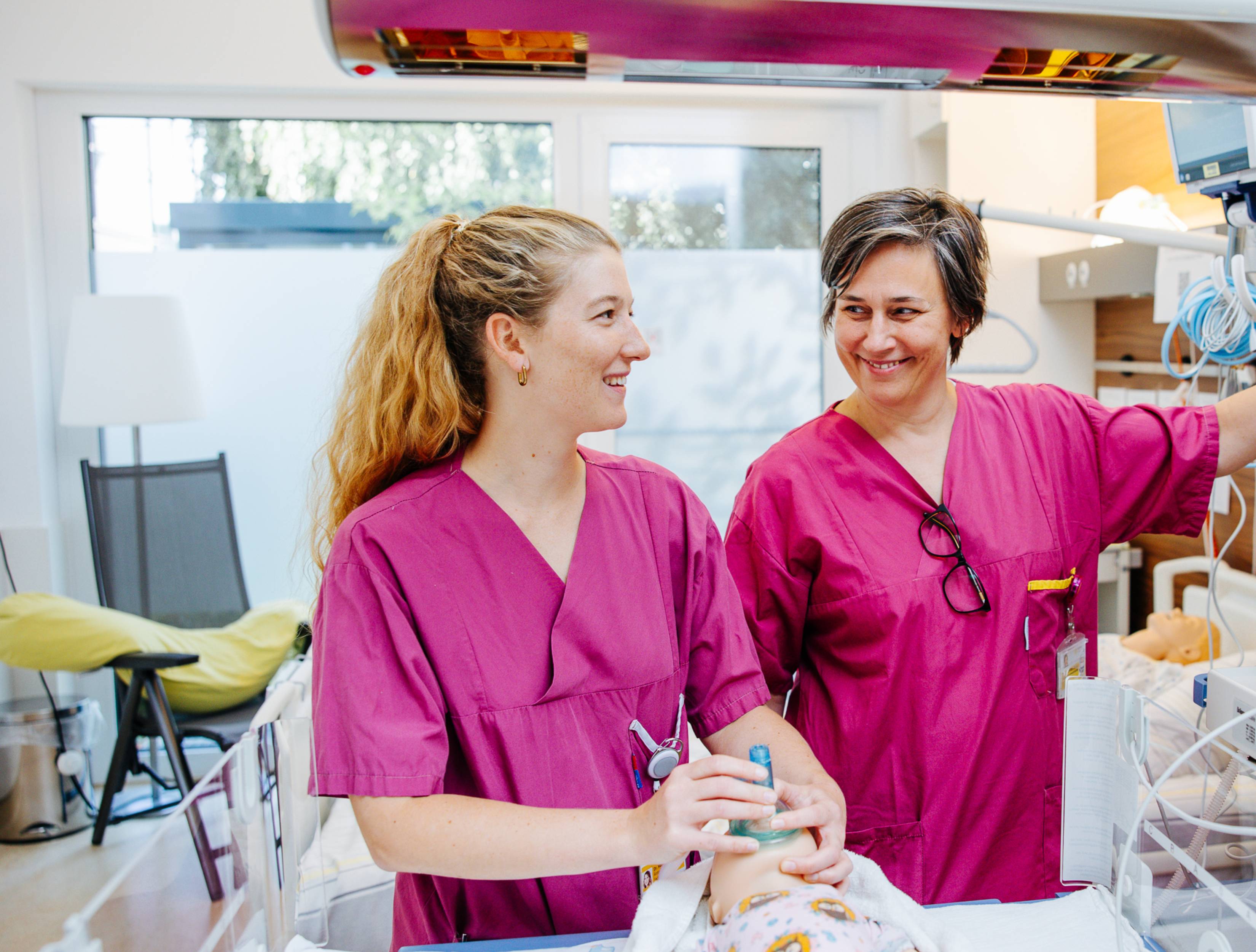 Zwei Pflegerinnen in rosa Krankenhausbekleidung üben an einer Babypuppe.