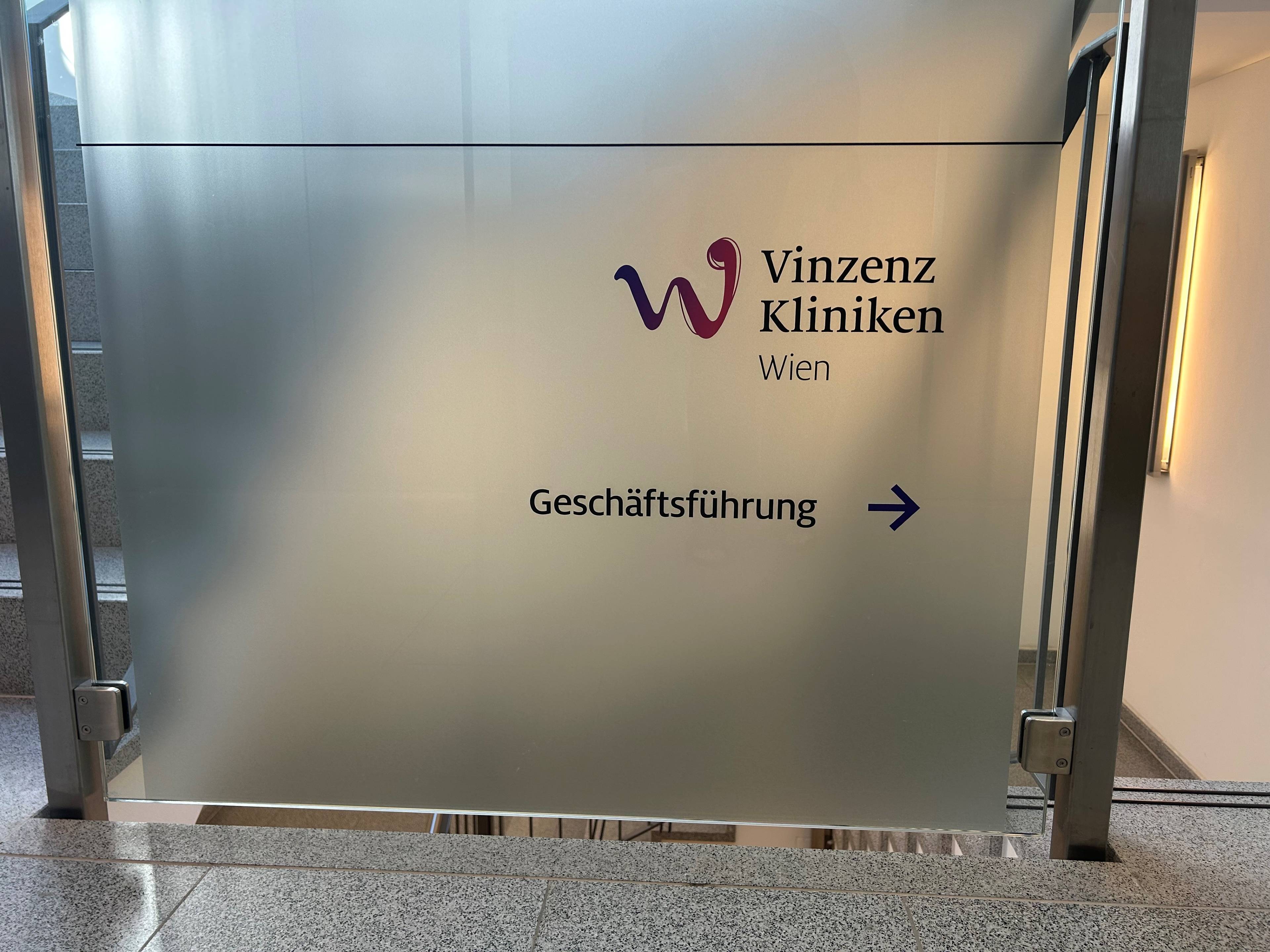Der Schriftzug "Vinzenz Kliniken Wien" auf einer Edelstahltafel in einem Stiegenhaus.