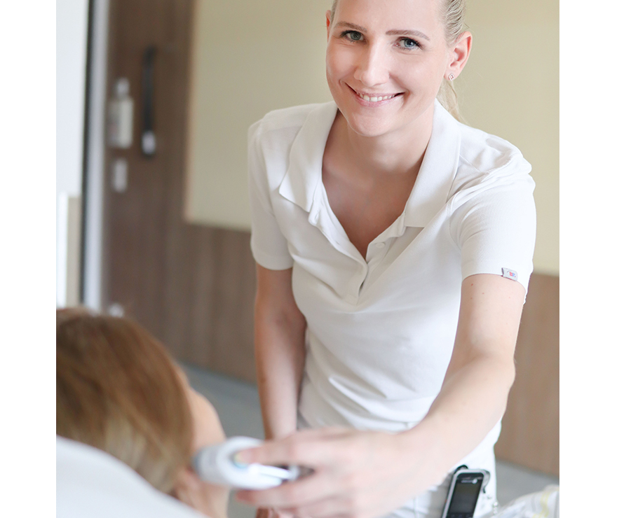 Eine Pflegerin misst einer Patientin am Ohr die Körpertermperatur