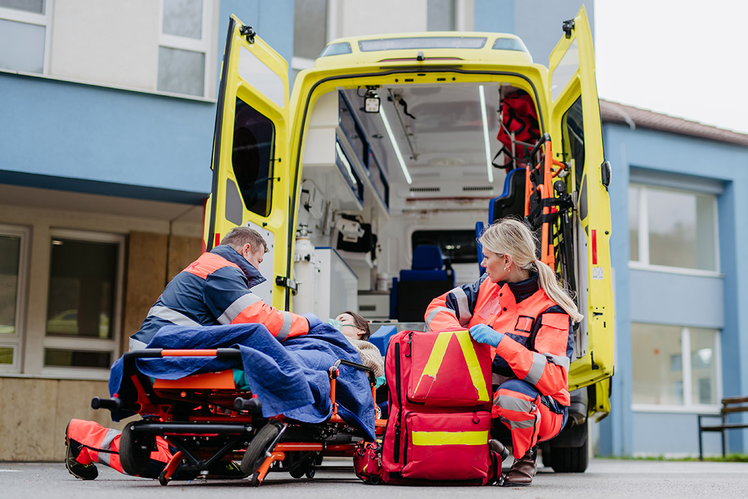 A patient on a stretcher being helped into a ground ambulance