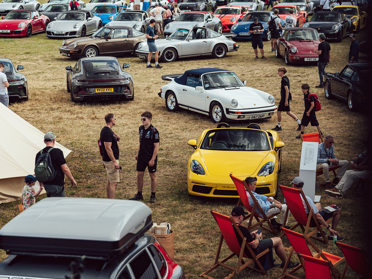 Ein vollgeparktes Gelände mit Menschen und diversen Porsche Fahrzeugen.
