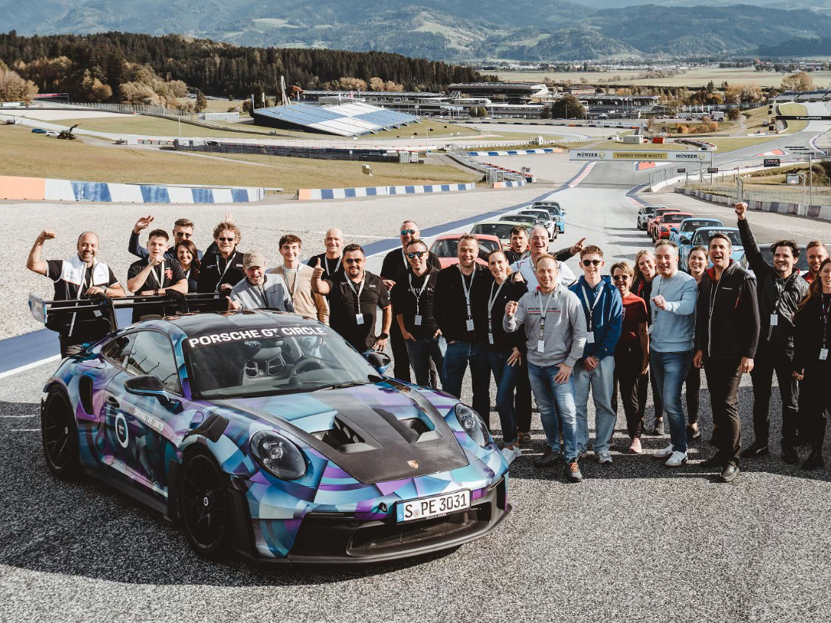 Porsche Fans posieren auf einer Rennstrecke mit einem Porsche 911 Rennfahrzeug.