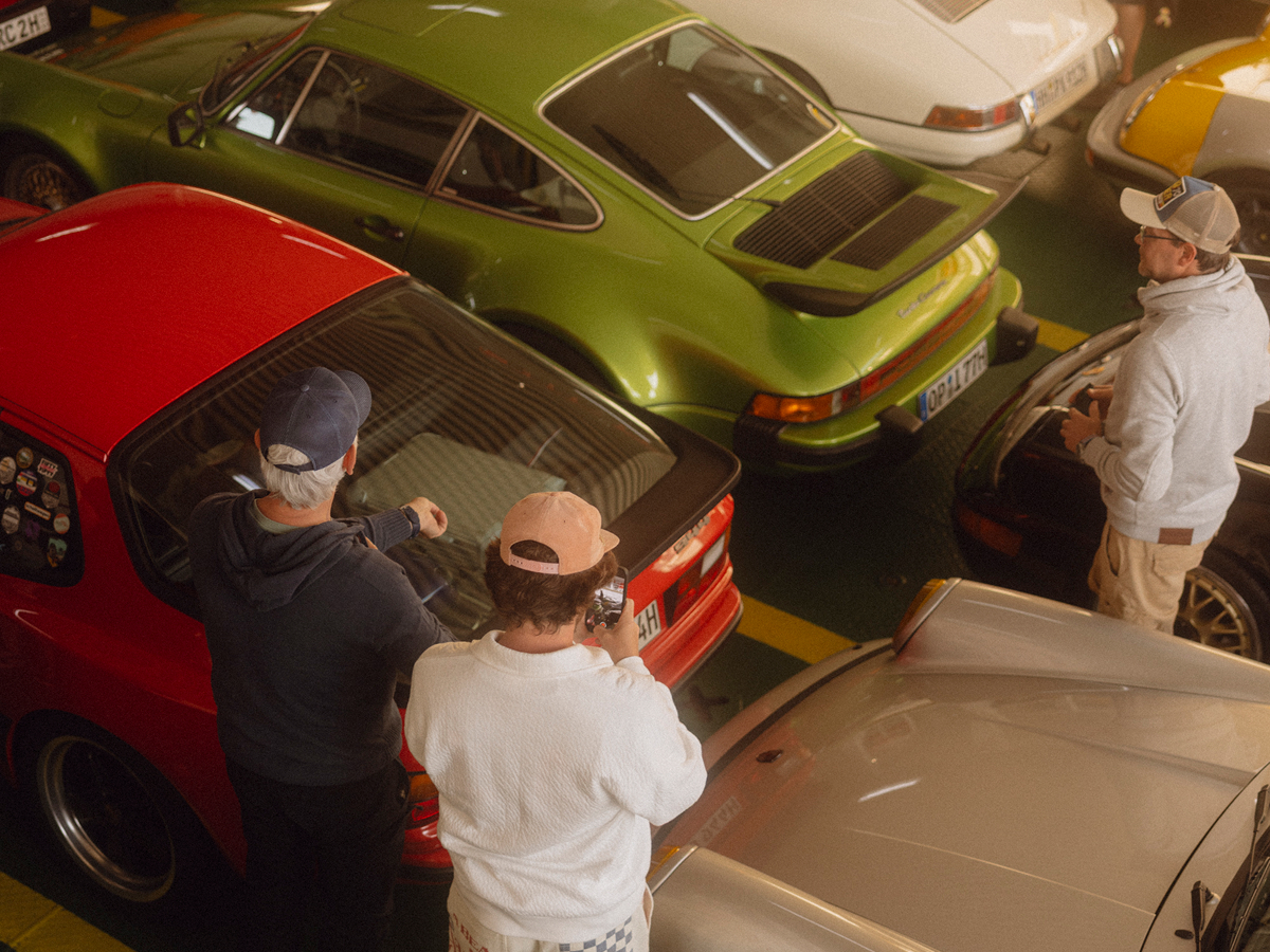 3 Männer stehen zwischen vielen klassischen Porsche Fahrzeugen und betrachten diese.