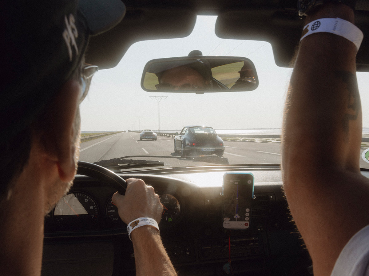 Blick aus dem Cockpit eines fahrenden Porsche auf die Straße, auf der weitere Porsche Fahrzeuge fahren.