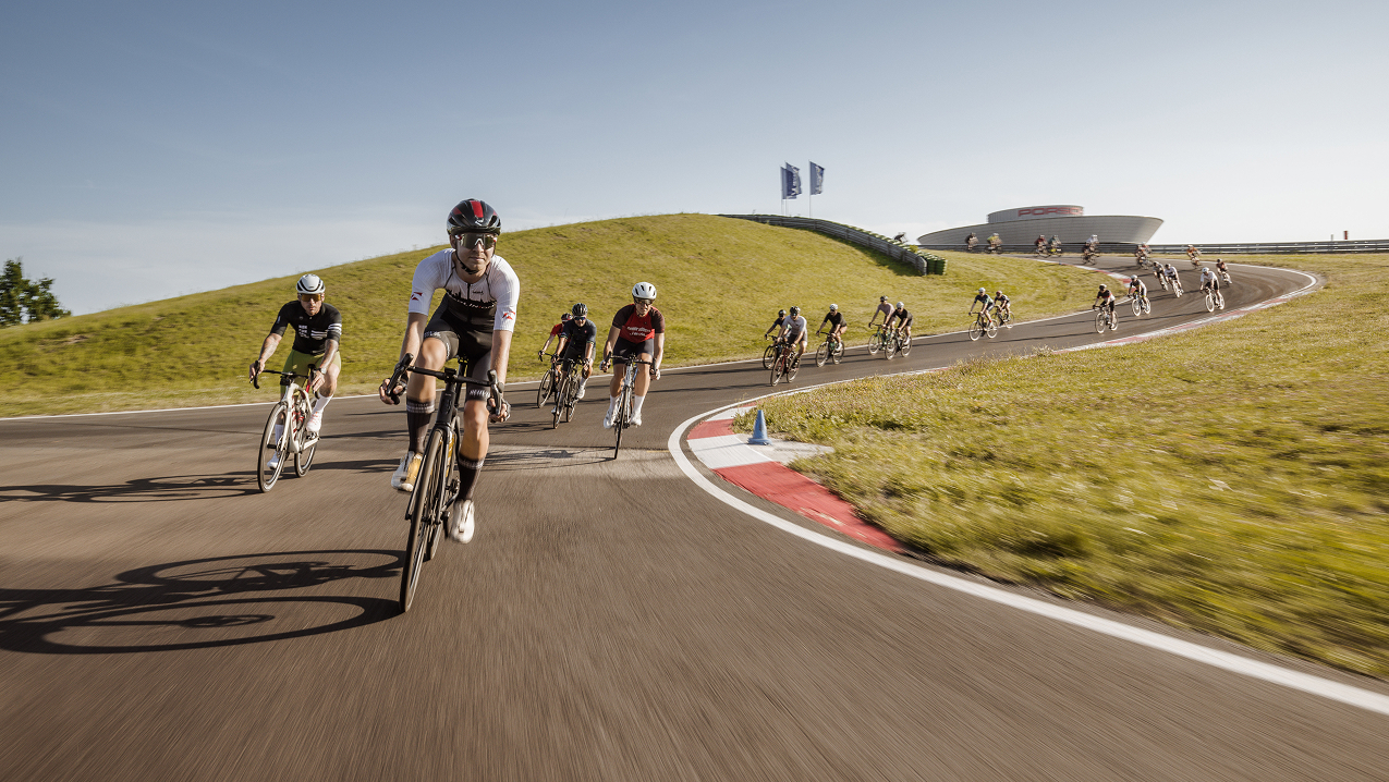 Blick von vorne auf eine große Gruppe Rennradfahrer, die auf einer Rundstrecke fahren.