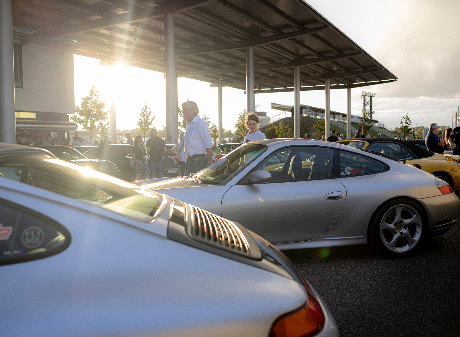 Diverse Porsche Modelle und Menschen stehen beim Porsche Experience Center Hockenheimring im Sonnenaufgang.