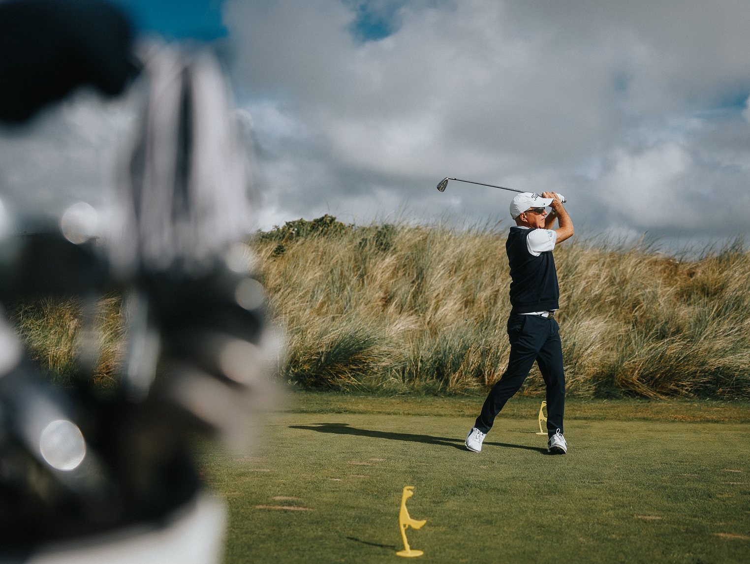 Ein Mann beim Golfen direkt nach dem Abschlag vor einer Wiese und bewölktem Himmel.