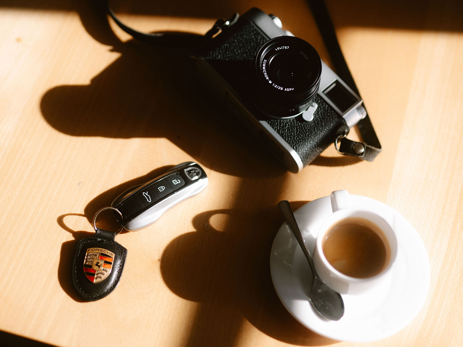 Ein Porsche Schlüssel, eine Kamera und ein Expresso liegen auf einem Tisch.