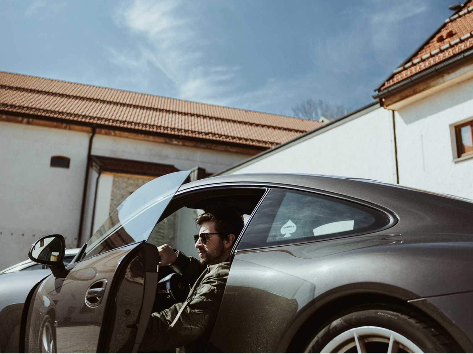 Ein Mann mit Sonnenbrille steigt aus einem Porsche aus.