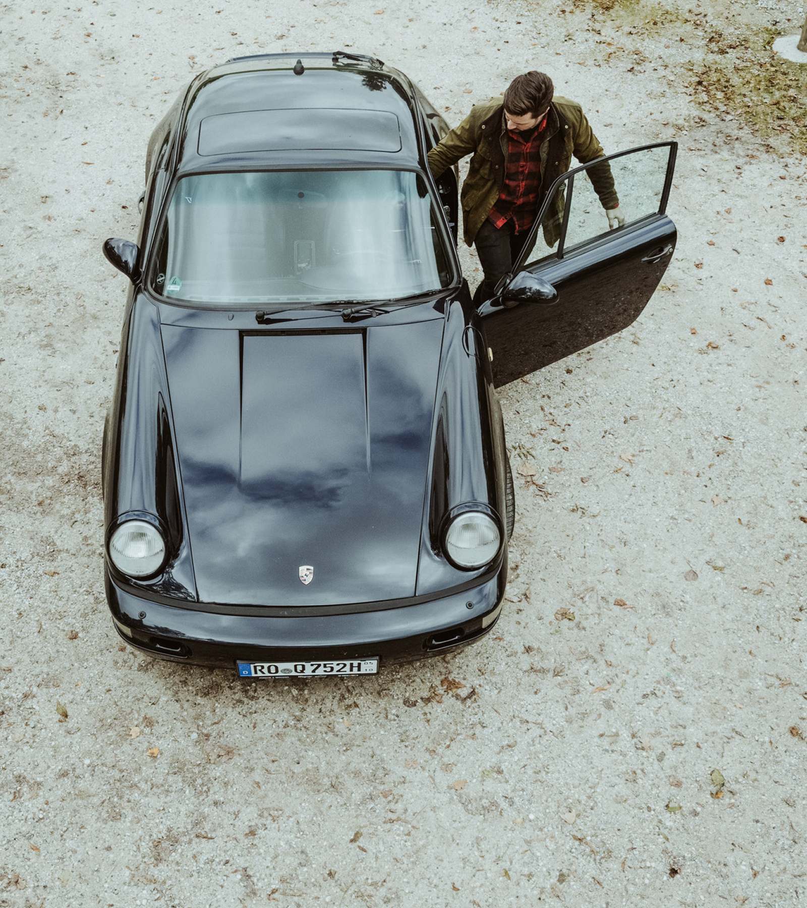 Ein Mann steigt in einen schwarzen Porsche ein, Blick von oben.