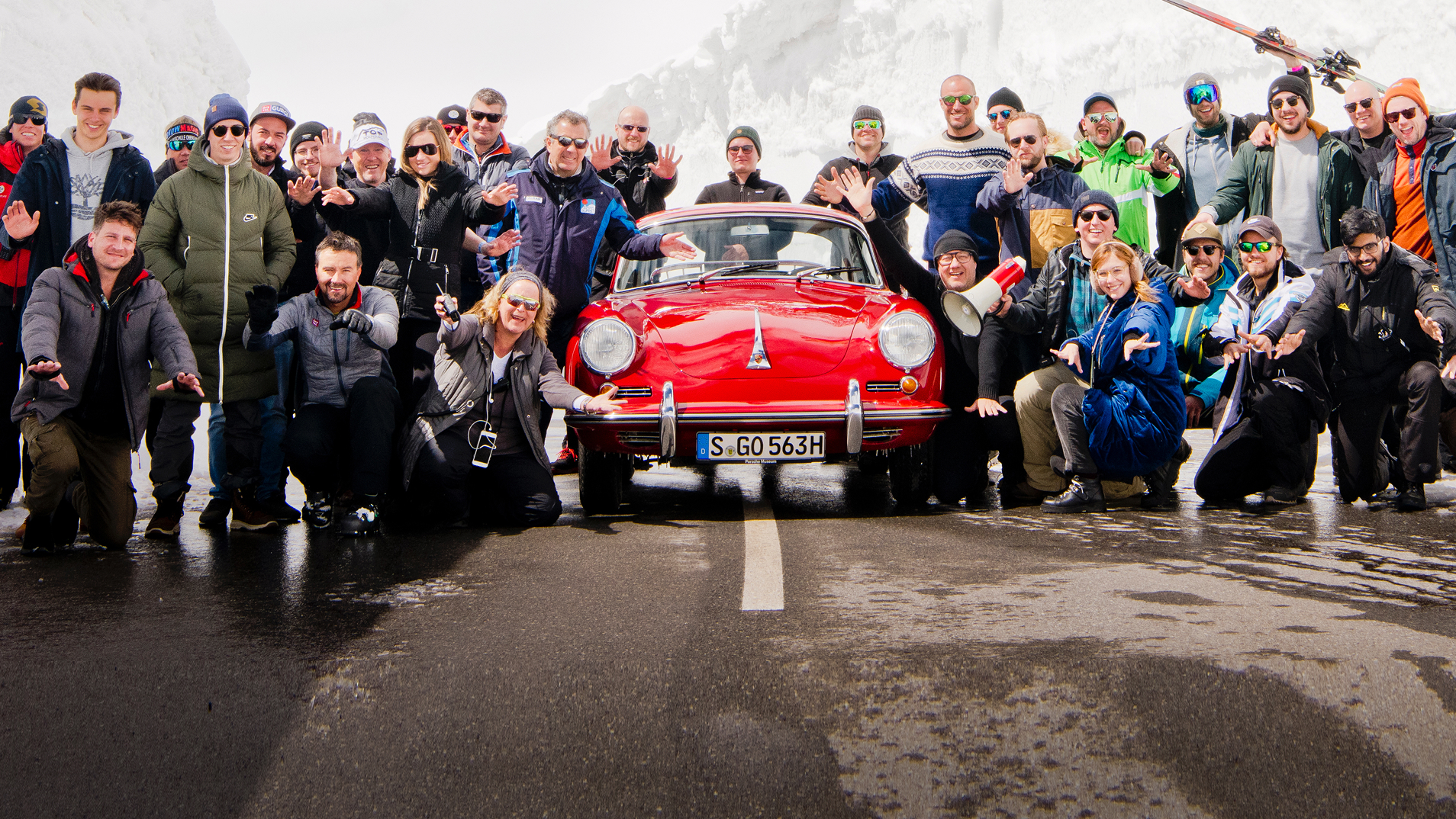 Porsche Fans posieren vor Winterkulisse neben einem klassischen, roten Porsche.