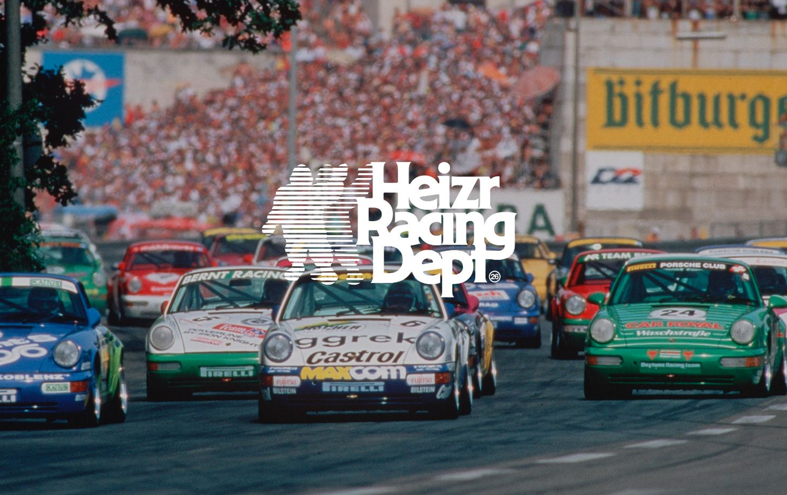 Mehrere bunte Oldtimer fahren auf einer Rennstrecke, in der Mitte steht Heizr Racing Dept.