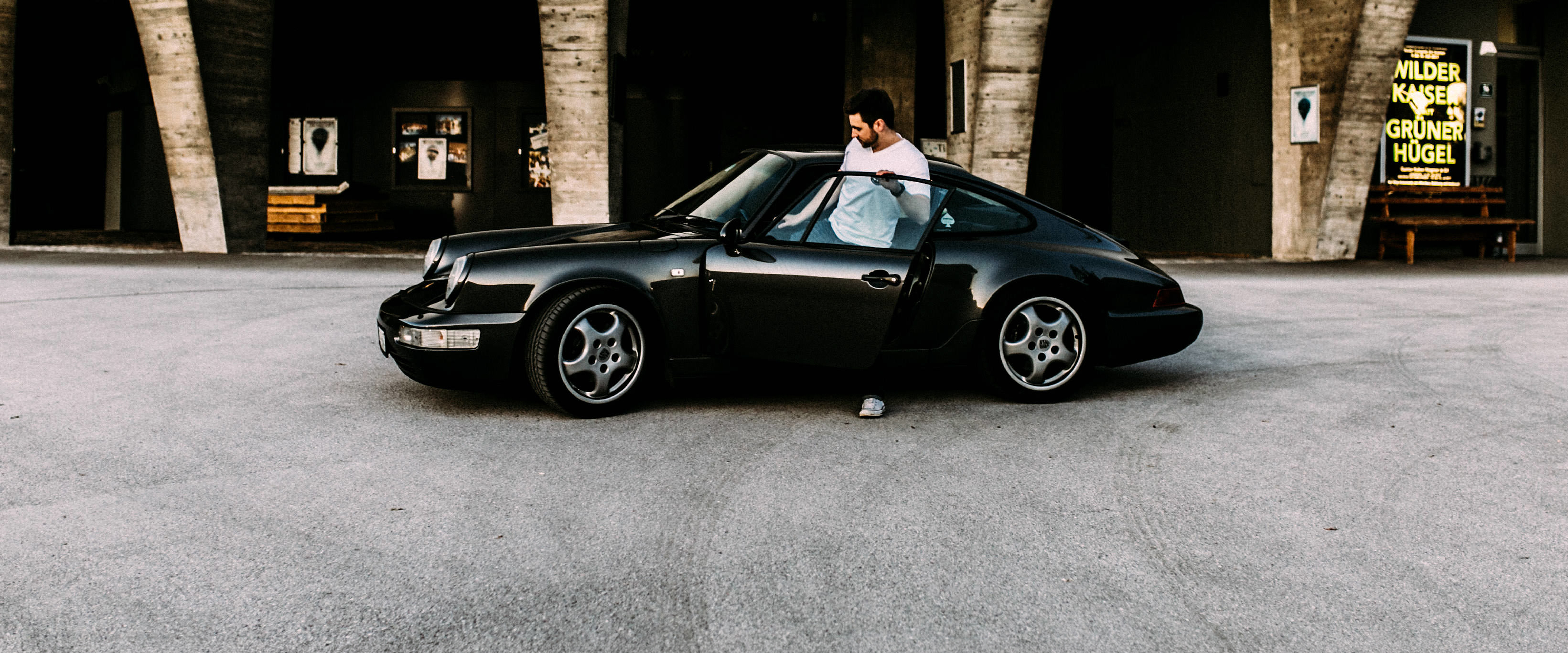 Ein Mann steigt in einen schwarzen Oldtimer Porsche ein.