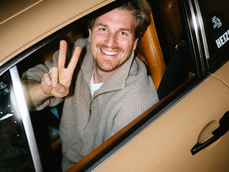 Ein lächelnder Mann zeigt aus einem klassischen Porsche heraus das Victory-Zeichen.