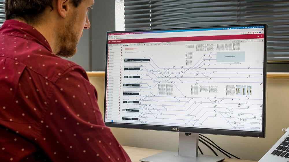 A man at an office desk, closely examining a complex asset diagram on a large computer monitor.