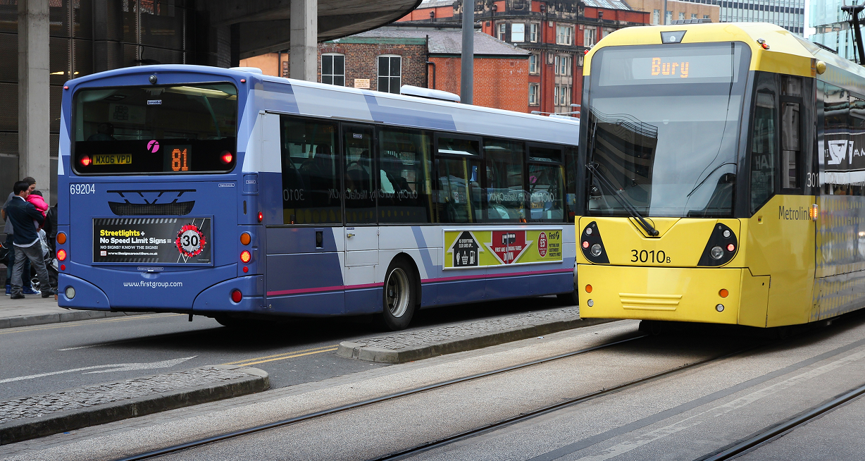 A blue bus and a yellow tram are side by side on a city street, with buildings in the background.