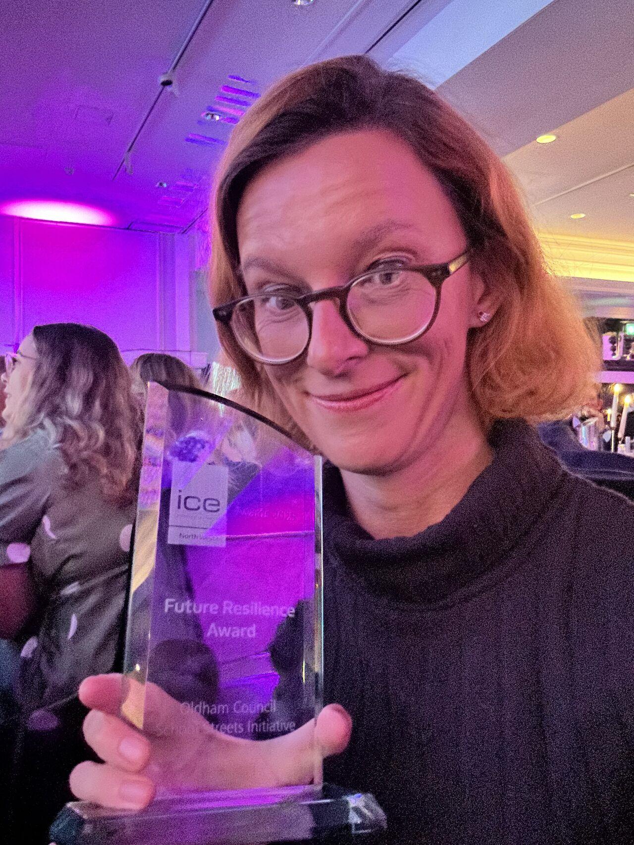 Person holding a "Future Resilience Award" trophy at an event, with a purple-lit background and attendees seated nearby.