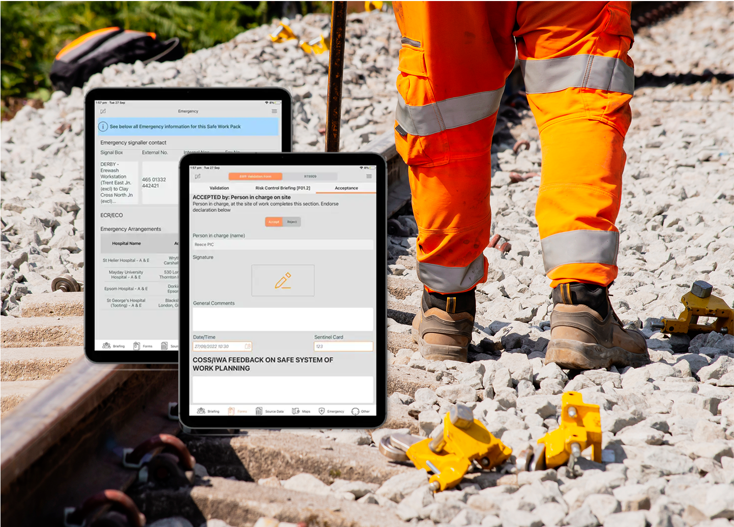 Worker in orange gear on railway tracks with two tablets displaying safety documents in the foreground.