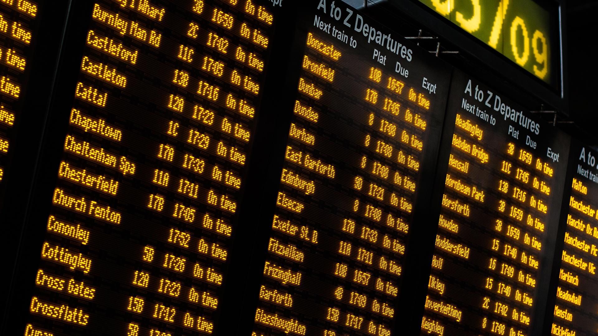 Close-up of a digital train departure board displaying various destinations, platform numbers, and times in bright yellow text on a black background.