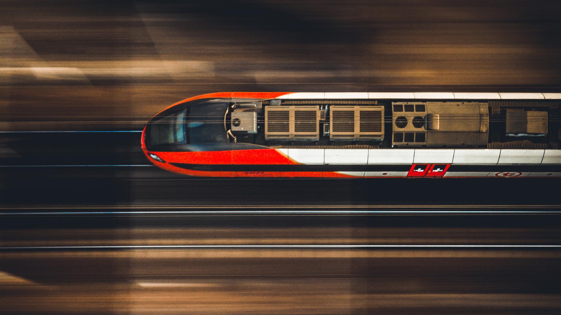 Aerial view of a speeding red and white high-speed train on blurred tracks, showcasing motion and modern design.