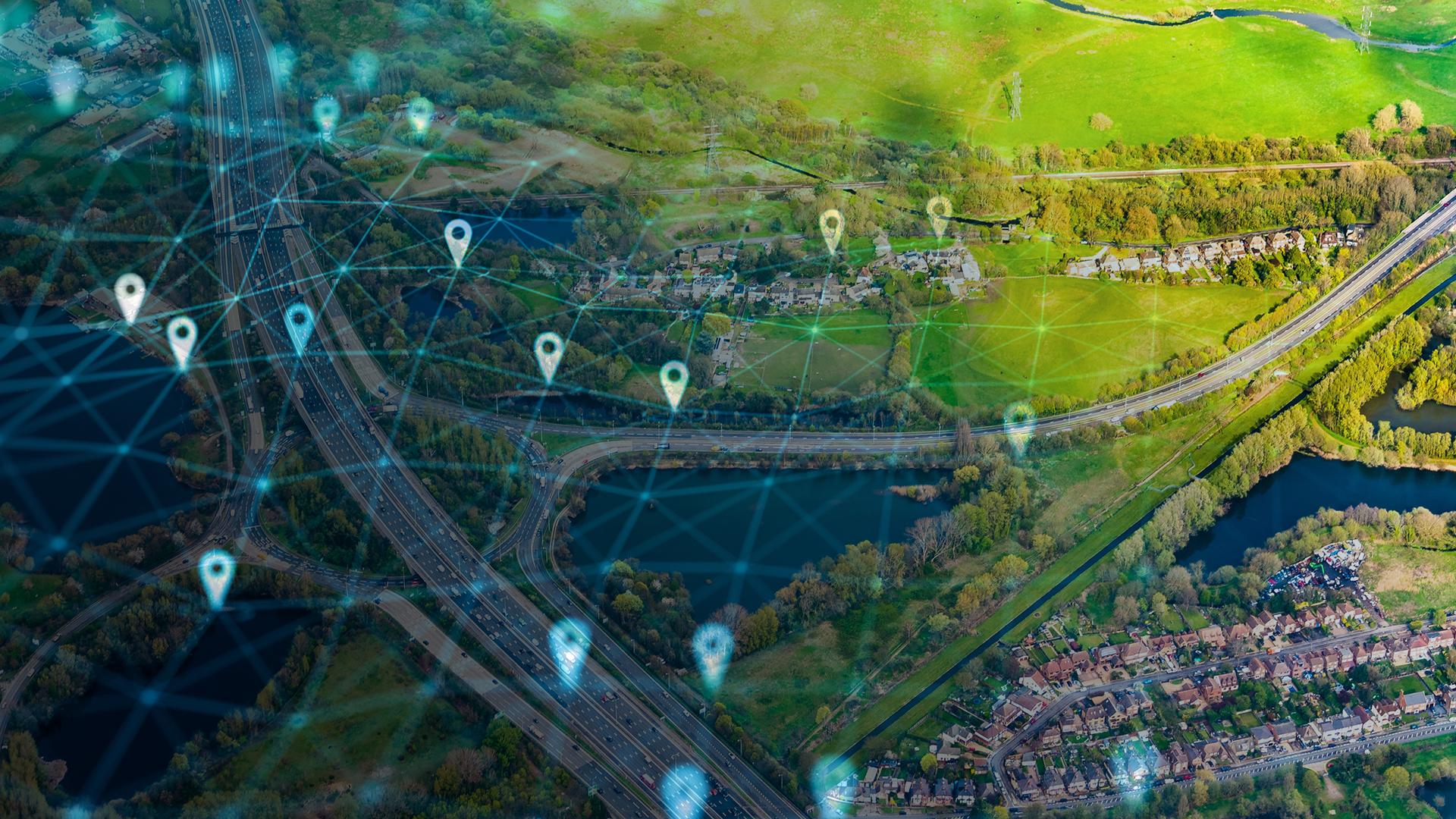 Aerial view of a landscape with digital location markers and network lines overlaying roads, fields, and residential areas.