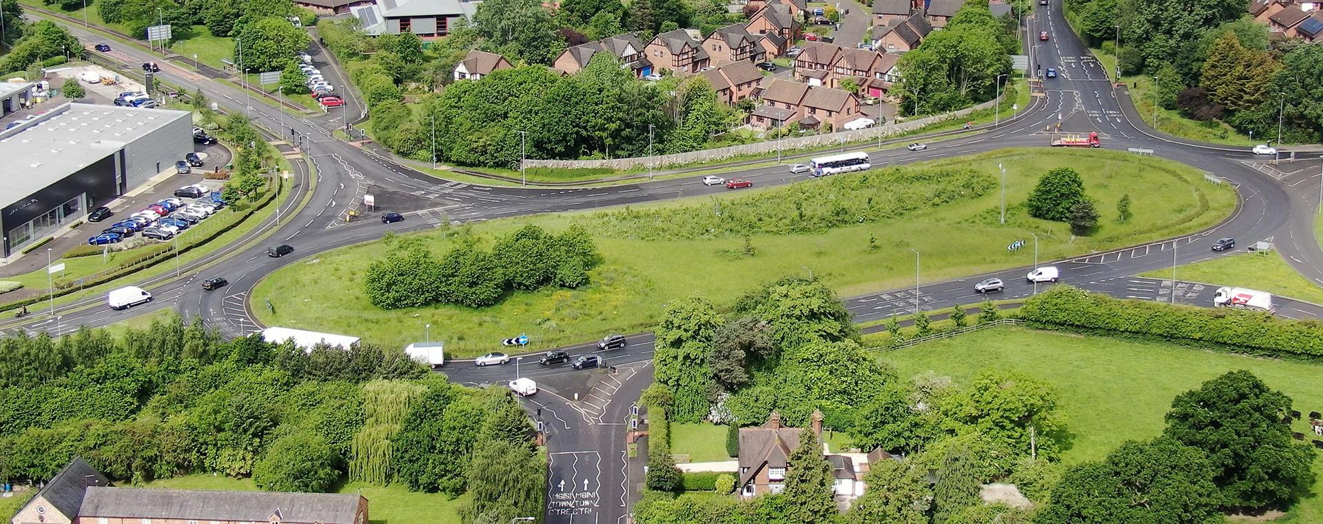 Aerial view of a large roundabout surrounded by greenery, houses, and a few vehicles on the roads.