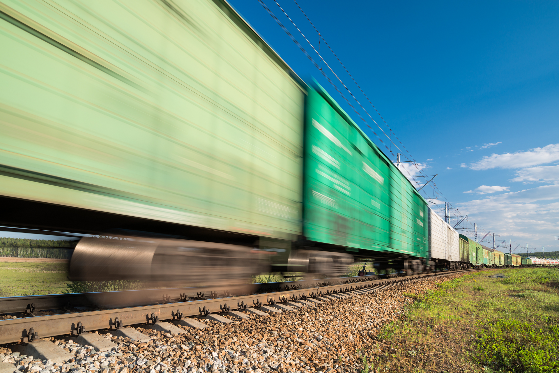 Green blurred rail freight wagons rapidly moving across a rail track.